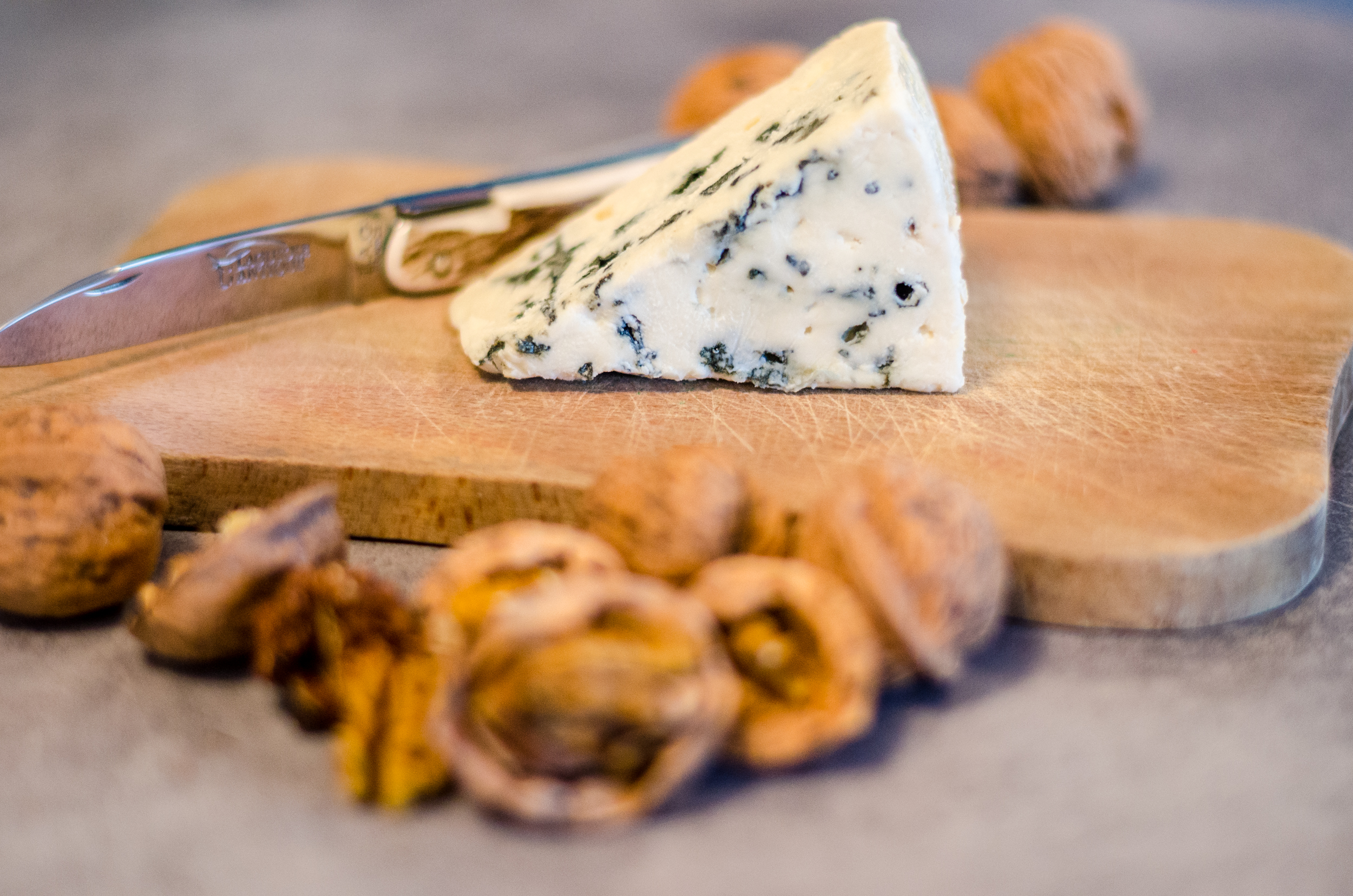 Tranche de Roquefort sur planche à découper avec couteau Laguiole moderne et noix